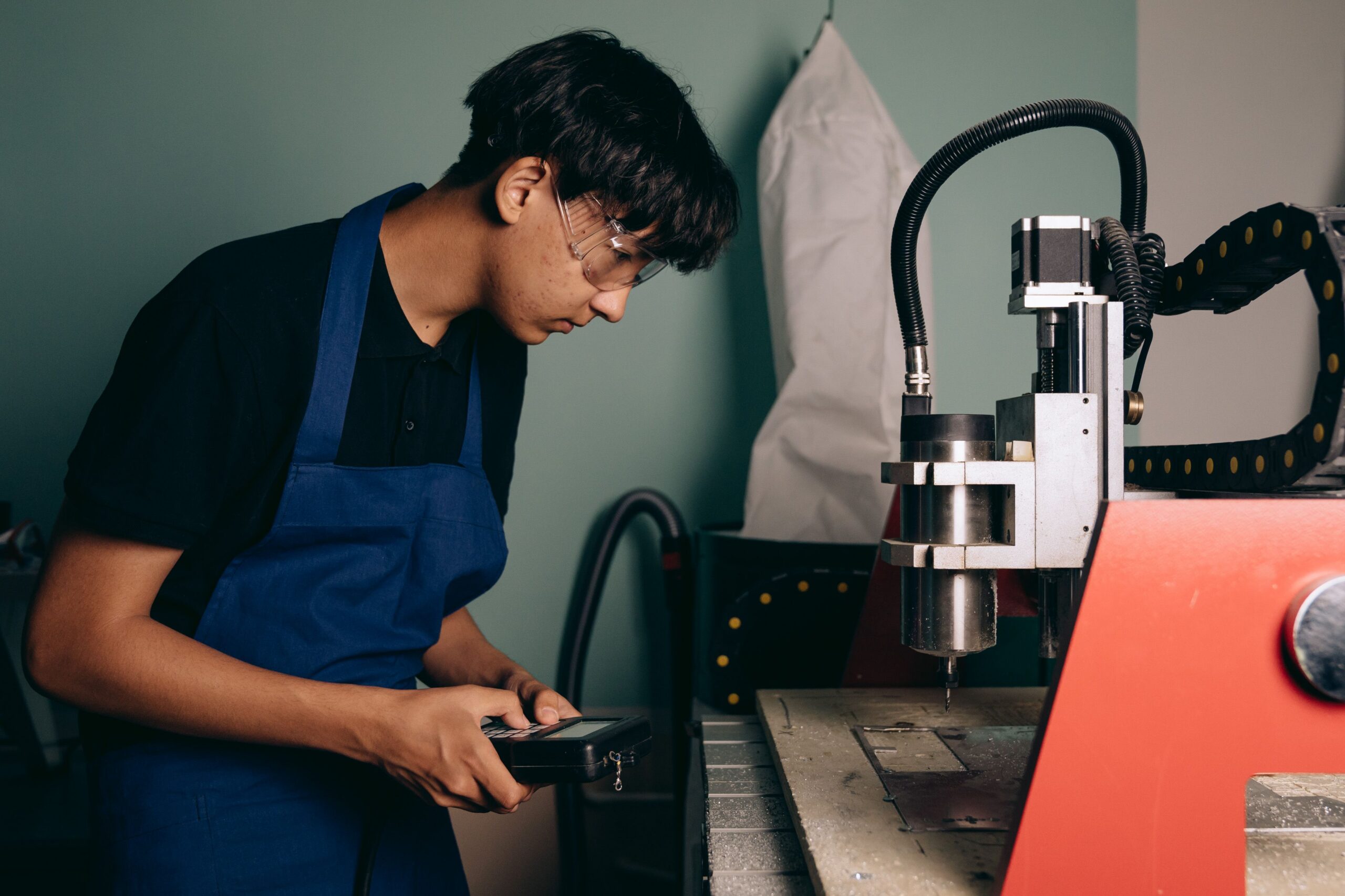 Người đeo kính bảo hộ theo dõi máy CNC bằng thiết bị điều khiển trong xưởng.