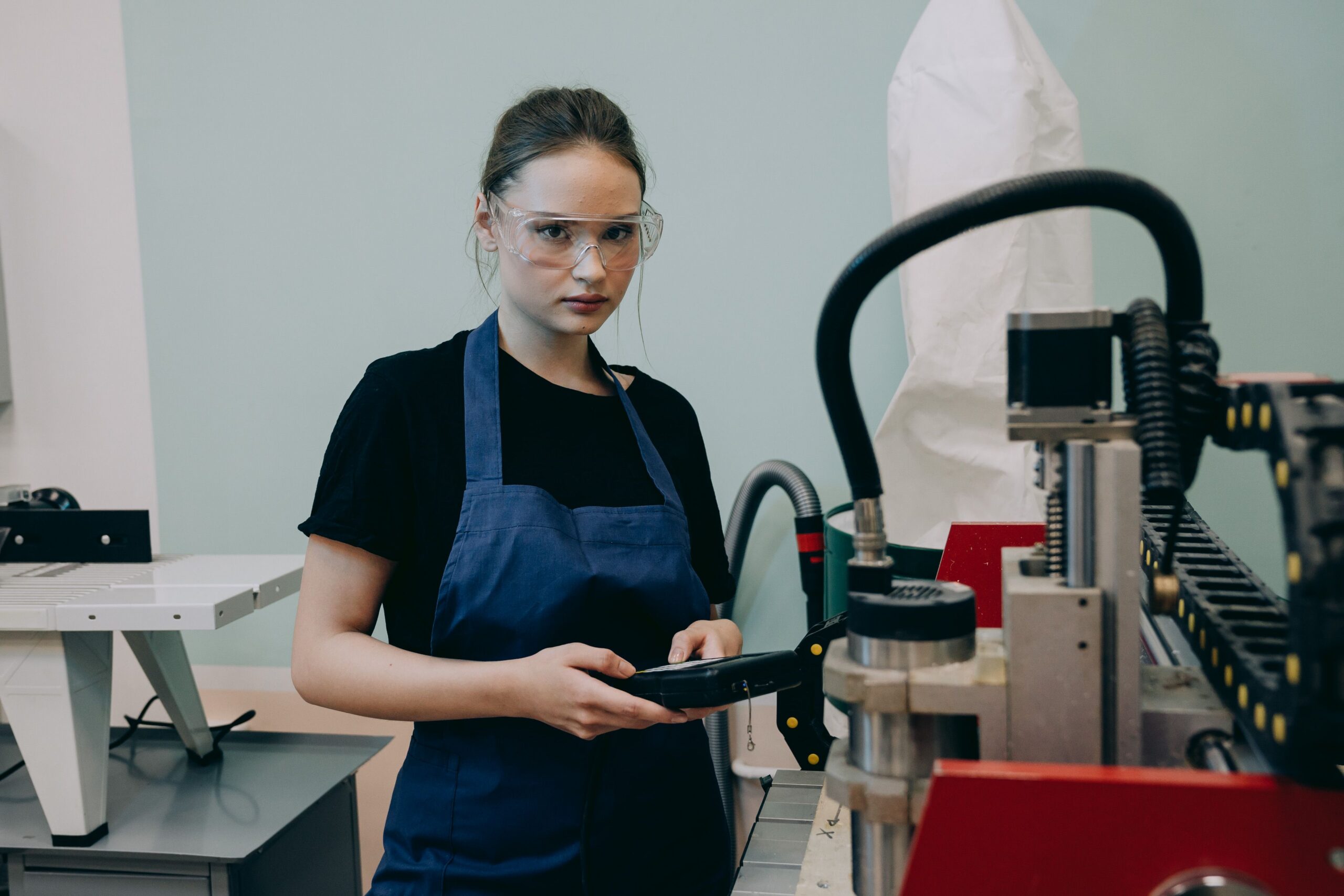 Một phụ nữ đeo kính bảo hộ cầm bộ điều khiển bên máy CNC.